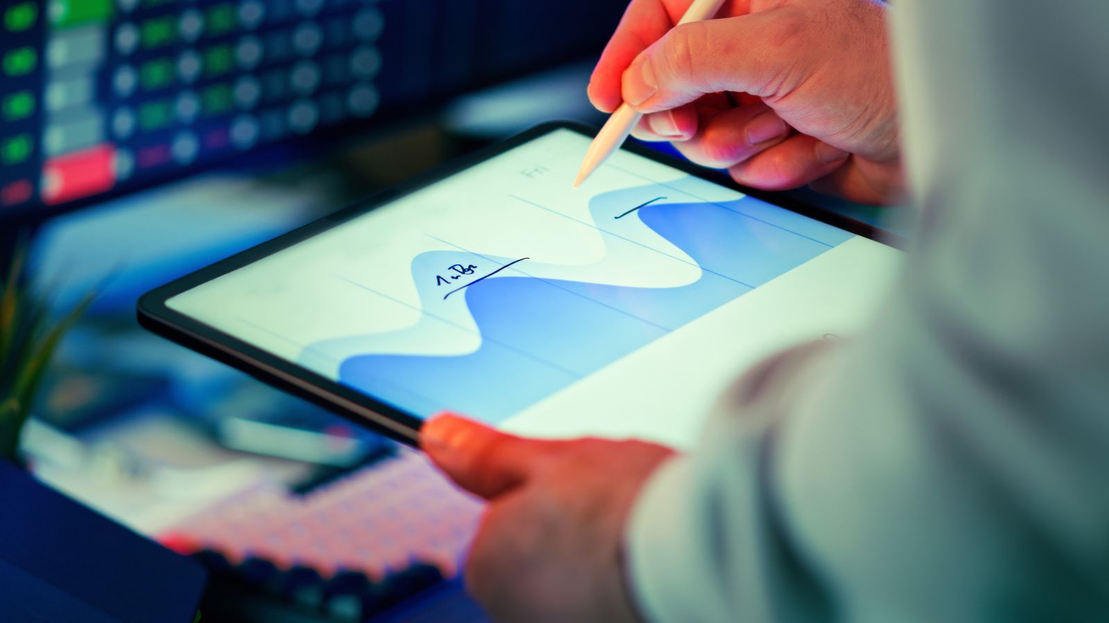 A hand using a stylus on a tablet to annotate a blue line graph, with blurred analytics screens in the background.