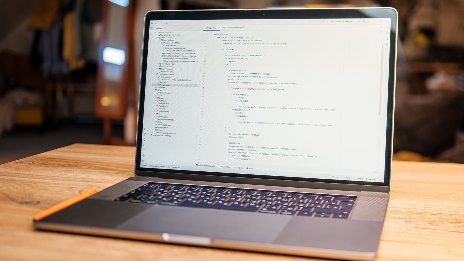 A laptop on a wooden desk displaying a code editor with source code open, in a softly lit workspace.